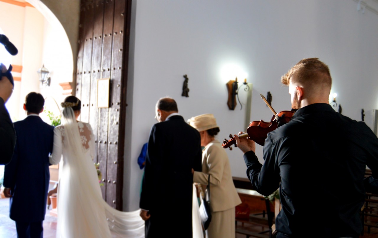 Una pareja de novios saliendo de la iglesia mientras suena la música de un violinista. 