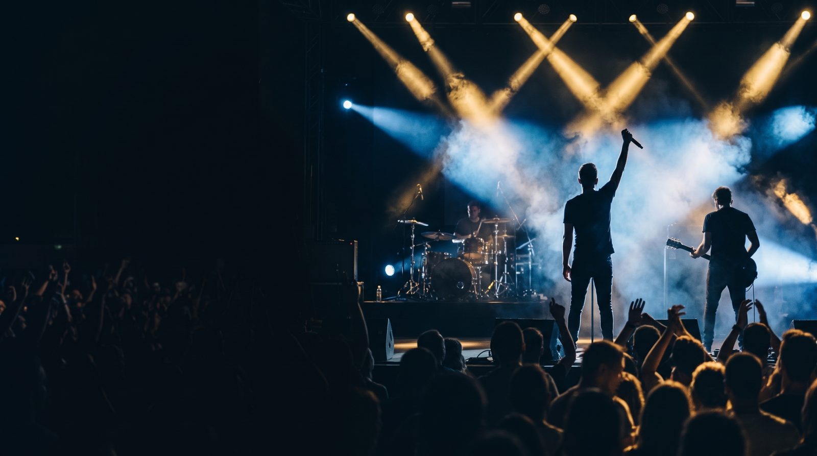 Banda tocando de noche en un gran escenario, con el cantante de espaldas saludando al público